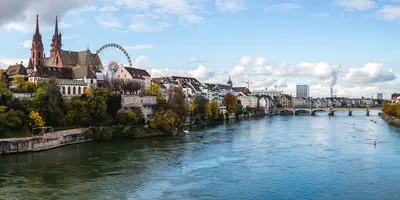 Panoramablick auf die Basler Uferpromenade – eine Stadt nahe der Schweiz, Deutschland und Frankreich – mit Kathedralen, zwei Türmen und dem Riesenrad.