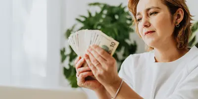 Frau sitzt vor einem Laptop und hält einen Haufen Bargeld in der Hand