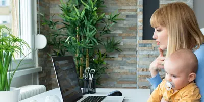 Mutter hält ihr Kind und arbeitet nebenher am Laptop