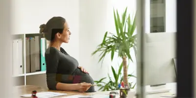 Schwangere Mitarbeiterin sitzt am Schreibtisch