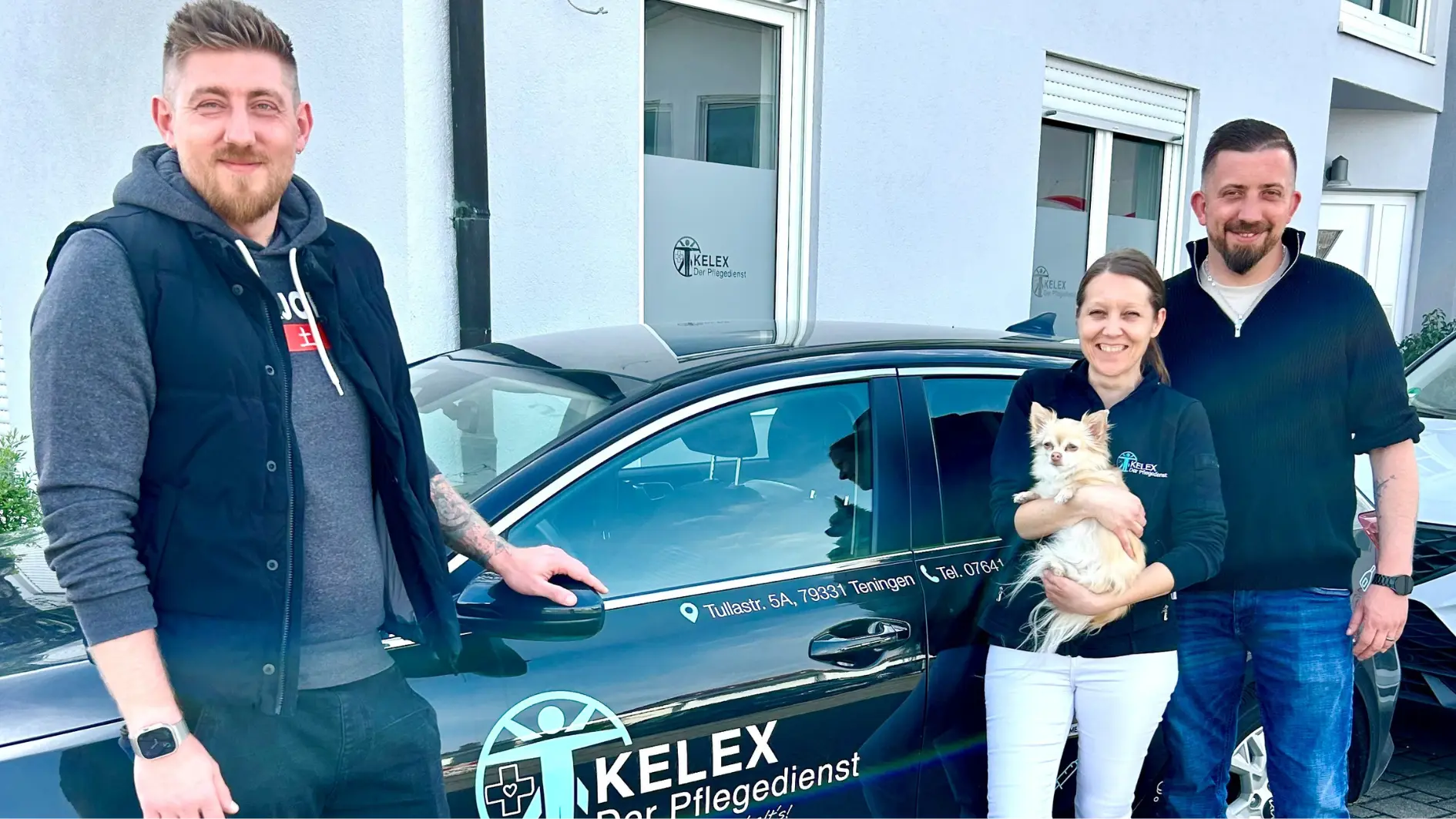 Drei Menschen mit einem Hund vor einem Auto
